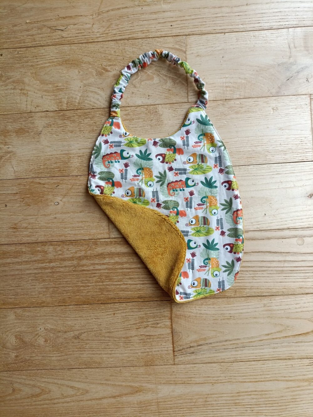 photo du bavoir bébé élastiqué avec motifs caméléons, doublé éponge de coton moutarde