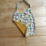 photo du bavoir bébé élastiqué avec motifs caméléons, doublé éponge de coton moutarde