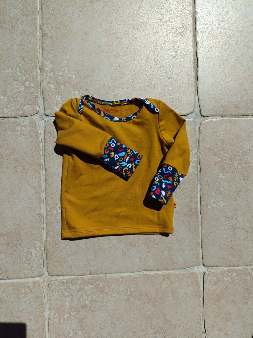 photo du tee-shirt évolutif bébé couleur moutarde et bordures colorées