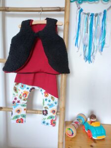 legging bébé et gilet de berger évolutifs posés sur cintre au milieu d'un décor de chambre d'enfant