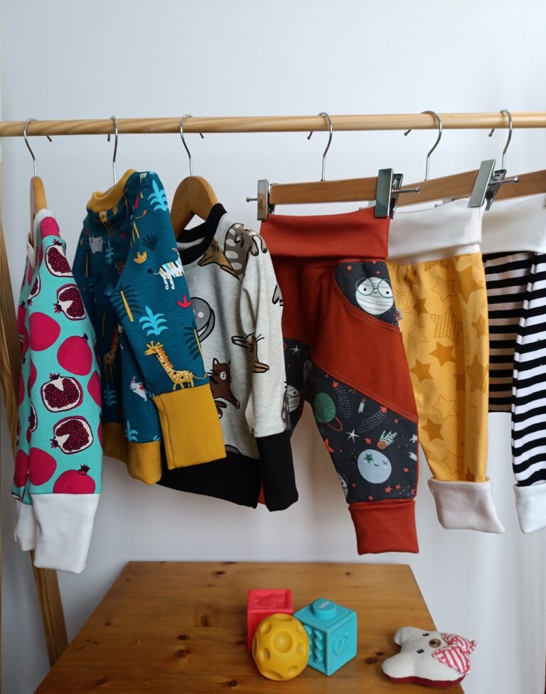 Plusieurs vêtements évolutifs colorés pour bébé et enfant, suspendus sur un portant dans l'atelier.