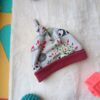 Baby hat with panda print and red brim resting on a soft white towel, with a teal spiky ball nearby