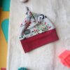 Knitted baby hat with panda print and red band on a soft light surface, with teal textured ball and pink blocks nearby.