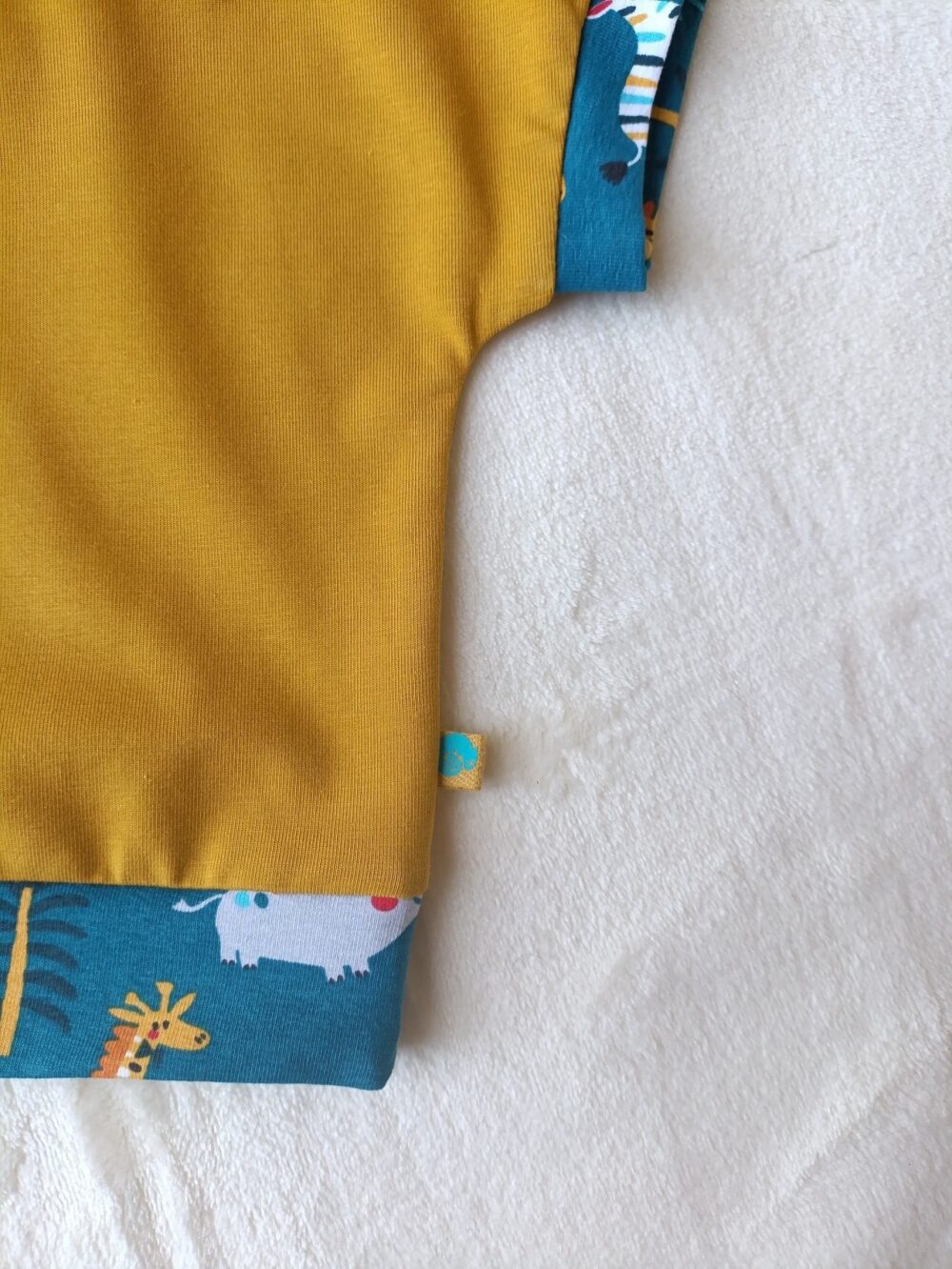 Close-up of a mustard-yellow fabric with a blue patterned edge featuring animals, against a light background.