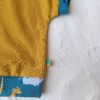 Close-up of a mustard-yellow fabric with a blue patterned edge featuring animals, against a light background.