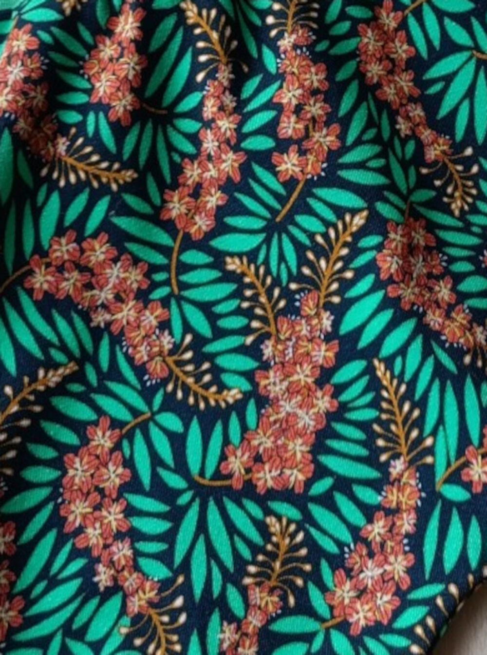 Close-up of a tropical floral pattern: pink blossoms with teal-green leaves on a dark background.