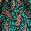 Close-up of a tropical floral pattern: pink blossoms with teal-green leaves on a dark background.