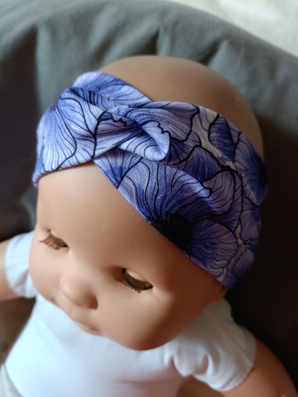 Bandeau large en tissu blanc à motif de grandes fleurs bleu et violet, croisé sur le devant. Présenté porté sur une poupée.