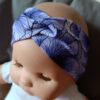 Bandeau large en tissu blanc à motif de grandes fleurs bleu et violet, croisé sur le devant. Présenté porté sur une poupée.
