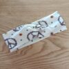 Bandeau en tissu blanc à motifs Peace & love, avec un nœud plat au centre. Modèle large de style croisé, présenté à plat sur un fond en bois clair.