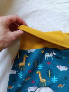 Détail de la ceinture moutarde d’un sarouel évolutif pour bébé, soulevée à la main pour montrer comment elle se replie et se déplie.
