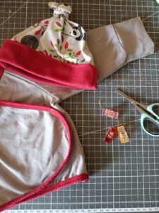 Coulisses de l’atelier : confection d’un vêtement pour bébé sur une table de coupe, avec ciseaux et pinces de couture.
